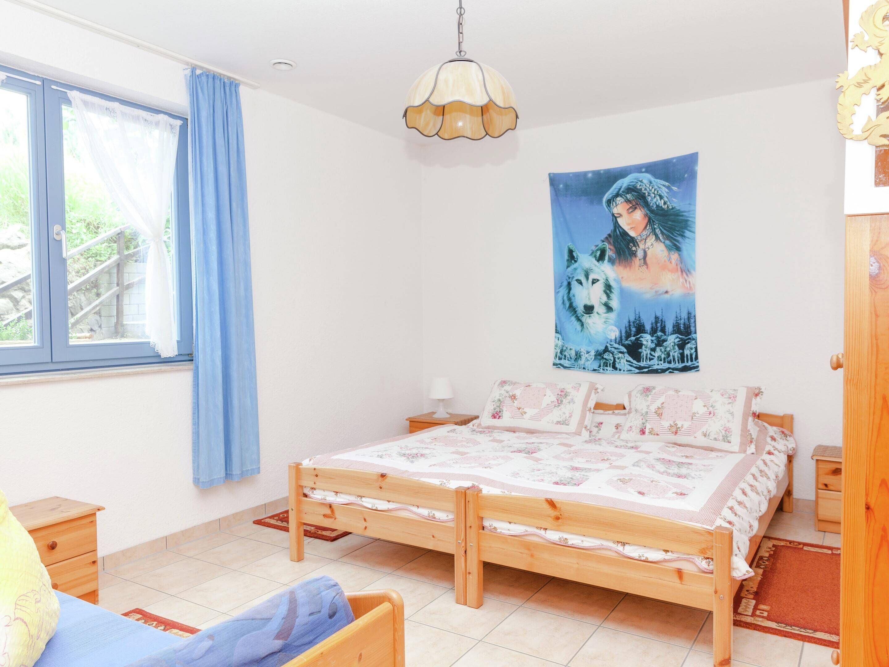 A bedroom with a wooden bed, a window with curtains, a wall tapestry, and a wooden nightstand.