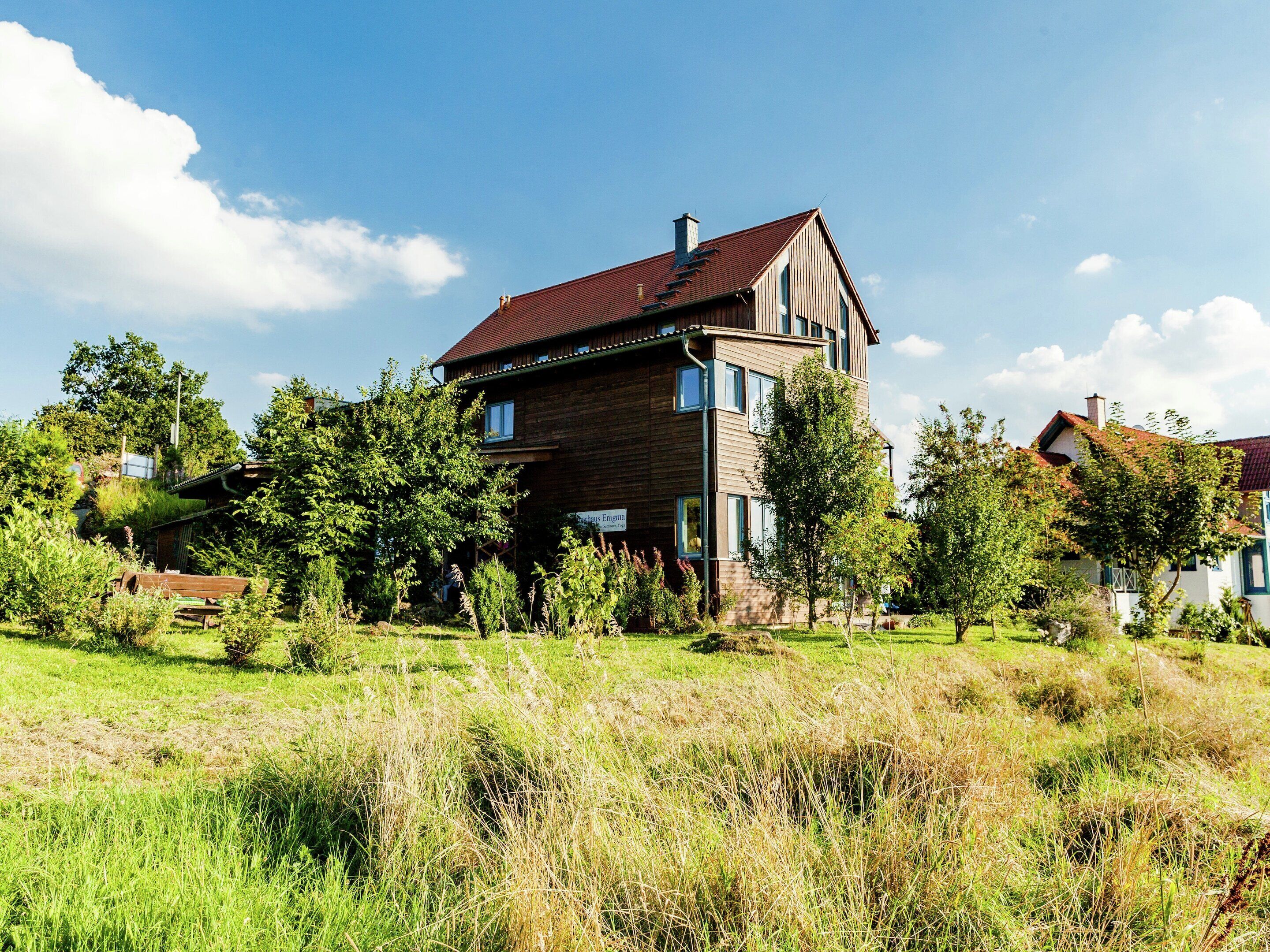 A two-story house with a red roof, surrounded by a grassy field and trees.