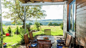 Une terrasse couverte avec une table et des chaises, une balançoire et une vue sur un paysage verdoyant.