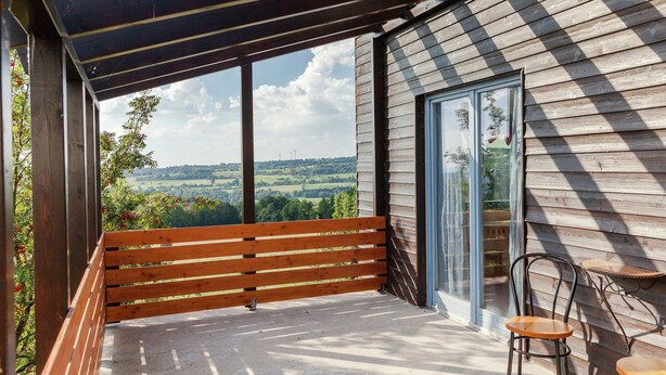 A wooden deck with a bench and two chairs, a glass door, and a view of the countryside. - Villa mit Sauna und Garten (Schotten)