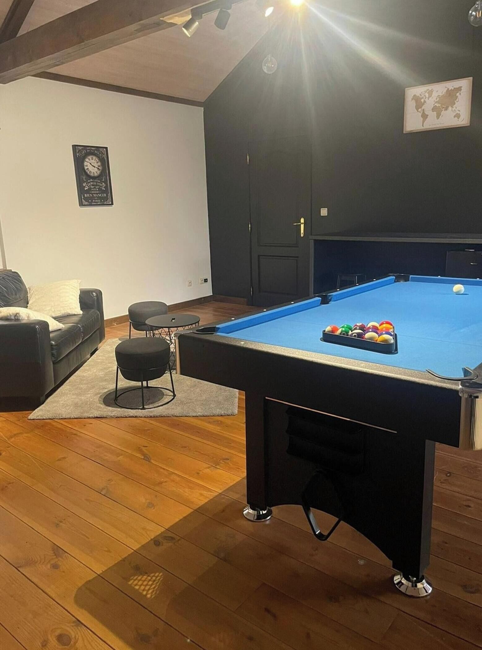 Ein Billardtisch mit Kugeln, eine Couch und ein kleiner Tisch mit einer Weltkarte an der Wand.
