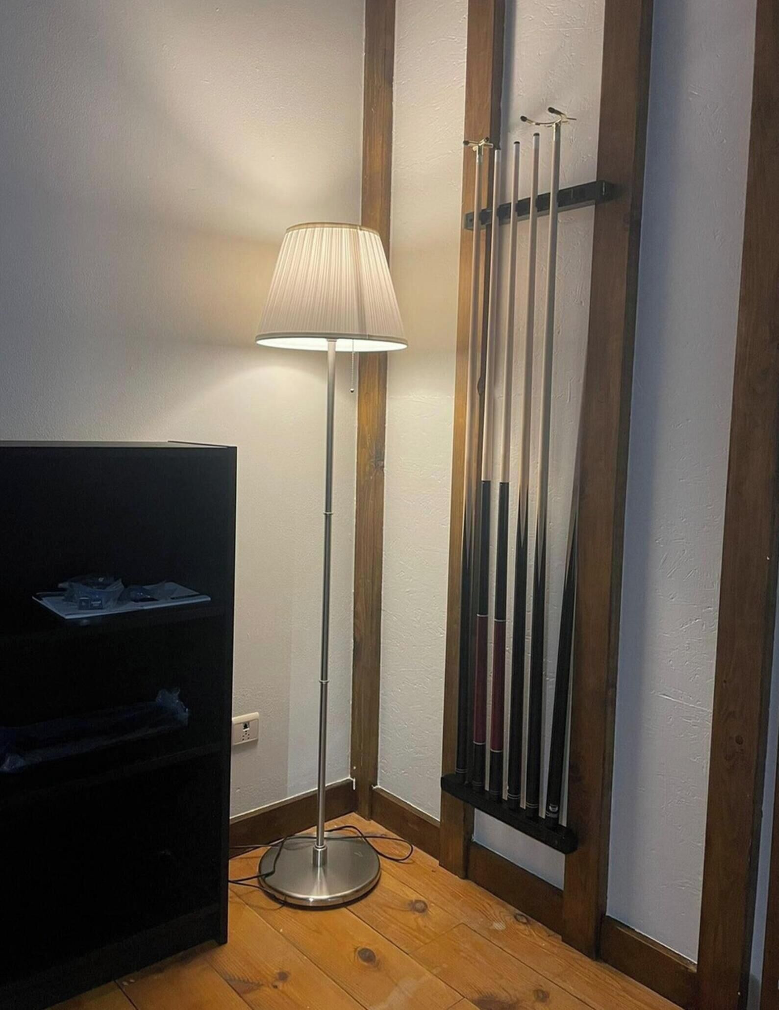 Una habitación de esquina con una lámpara de pie, un mueble para televisión y un estante vertical con objetos.