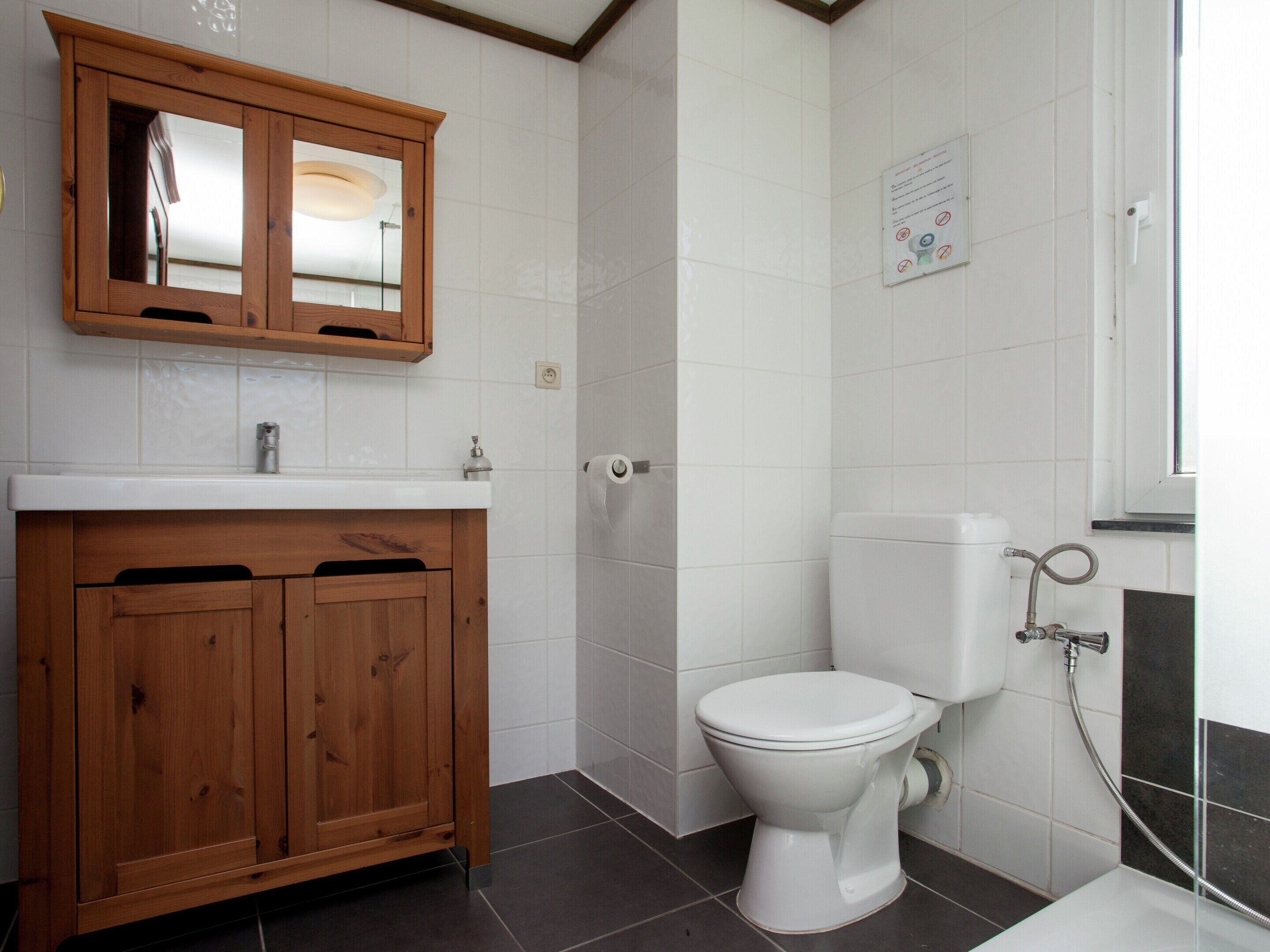 Une salle de bain avec un meuble en bois, des toilettes et une douche.