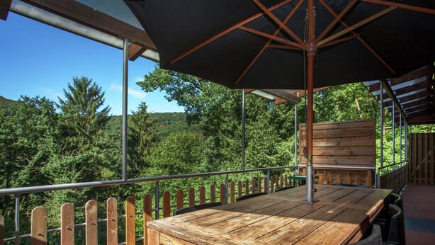 A wooden deck with a table and chairs, overlooking a forested area.