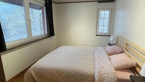 A bedroom with a bed, two windows, a ceiling light, and a nightstand with a lamp.