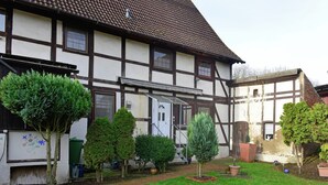 Une maison traditionnelle à colombages, dotée d’un jardin bien entretenu et d’un chemin d’accès dégagé menant à l’entrée.