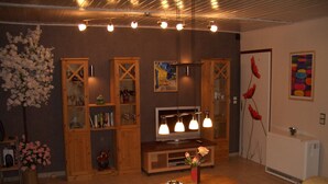 Un salon comprenant une table basse en bois, un canapé et un meuble pour la télévision avec un téléviseur à écran plat. On y trouve également des armoires en bois avec des portes en verre, un lustre et une œuvre d’art accrochée au mur.