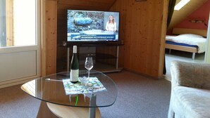 Une pièce avec une table en verre, une bouteille de vin et un téléviseur diffusant un journal télévisé.