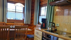 A wooden cabin interior with a dining area, kitchen, and a window with curtains. - Comfort & Nature in Dankerode (Harzgerode)