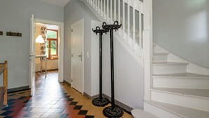 A hallway with a staircase, a coat rack, and a door leading to another room. - Rustic Ardennes Retreat (Vielsalm)