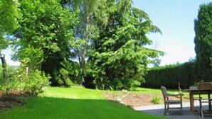 A well-maintained garden with a lawn, a wooden bench, and a table, surrounded by various trees and shrubs. - Rustic Ardennes Retreat (Vielsalm)