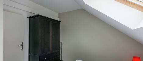 Ein Schlafzimmer mit Oberlicht, Kleiderschrank, Bett und Nachttisch in Rot.