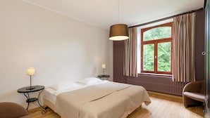A bedroom with a bed, a chair, a lamp, a window with curtains, and a radiator. - Rustic Ardennes Retreat (Vielsalm)