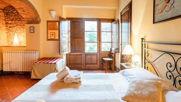 Une chambre confortable avec un grand lit, une porte en bois donnant sur un balcon et un mur en pierre.