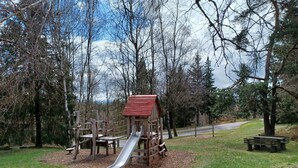Um parquinho com escorrega e estruturas de escalada, rodeado por árvores.