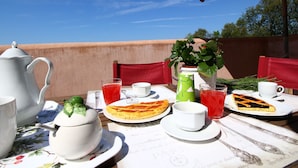 Une table à manger installée à l’extérieur, dressée avec divers plats, dont une pizza et une salade de fruits, le tout sur fond de ciel bleu azur.