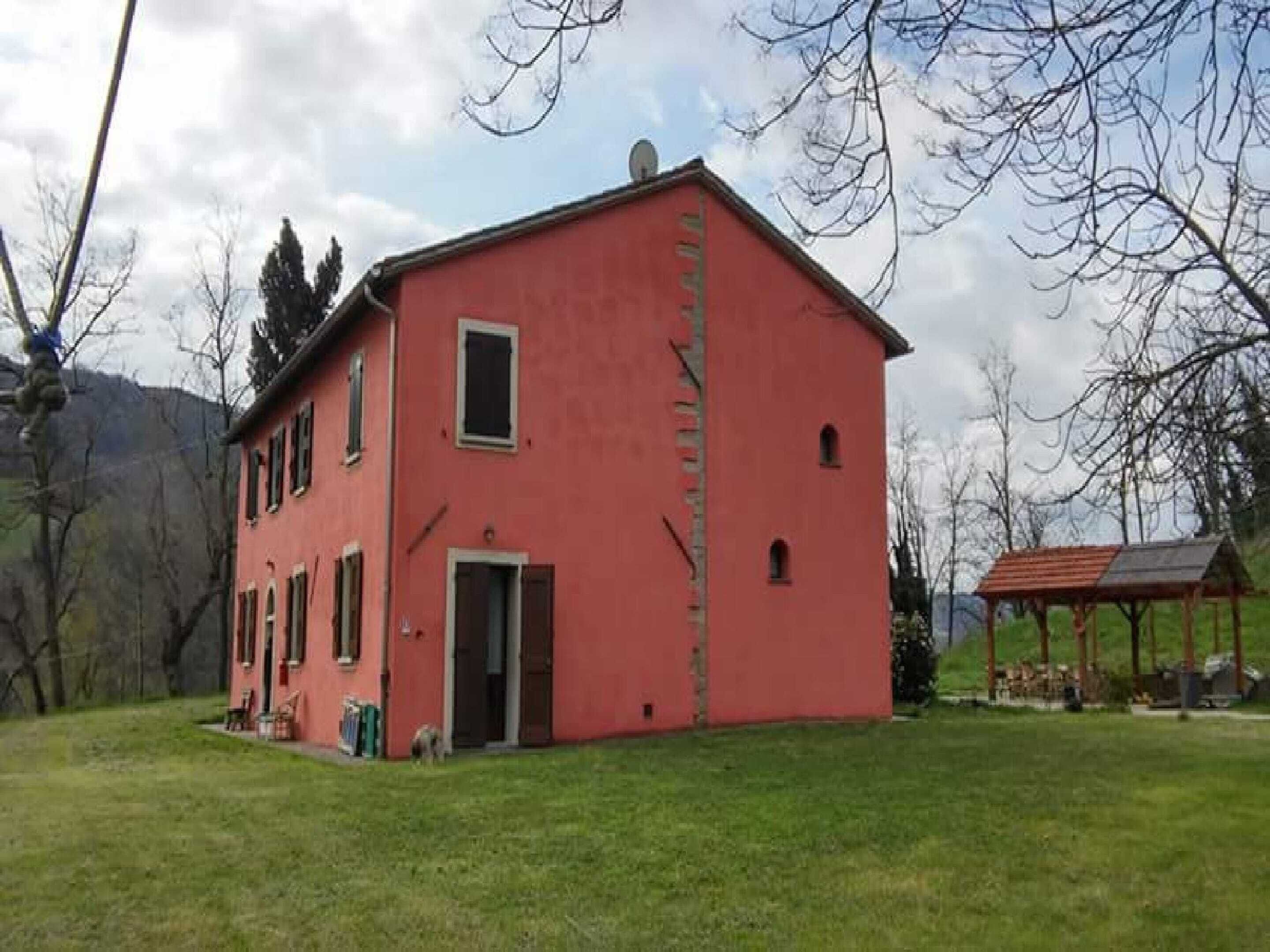A red building with a door and windows, surrounded by grass and trees.