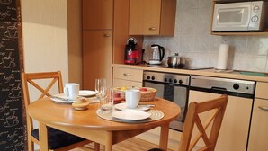 Una piccola cucina con mobili in legno, un forno a microonde, una macchina da caffè e un tavolo da pranzo apparecchiato con piatti, bicchieri e un cesto di limoni.