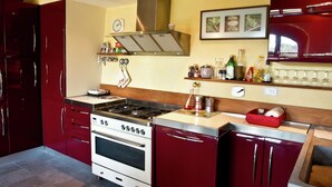 Een keuken met een fornuis, oven en rode kasten. Er hangt een klok aan de muur en een plank met diverse spullen.