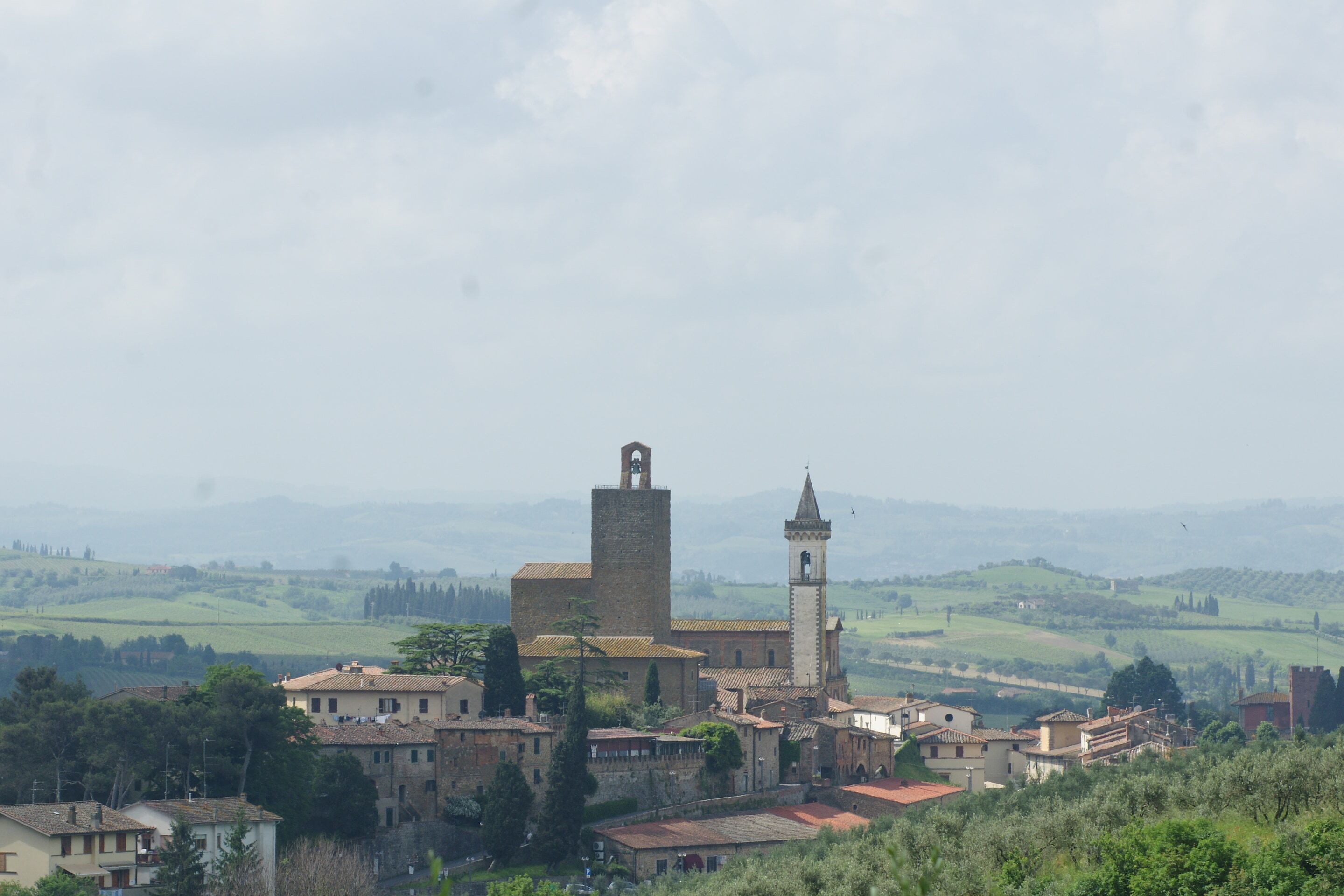 A historic town with a prominent church featuring a bell tower, surrounded by lush greenery and rolling hills in the background.