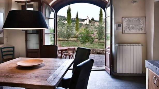 Een eethoek met een houten tafel en stoelen, een zwarte lamp en een uitzicht door een open poort naar buiten.