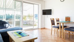 A modern living room with a sofa, a small table with a mat, a TV mounted on the wall, and a dining area with chairs and a table.