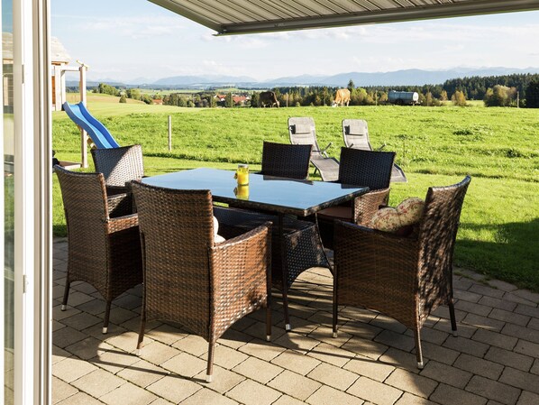 Relax on the patio with a refreshing drink, surrounded by a serene grassy field and breathtaking mountain views.