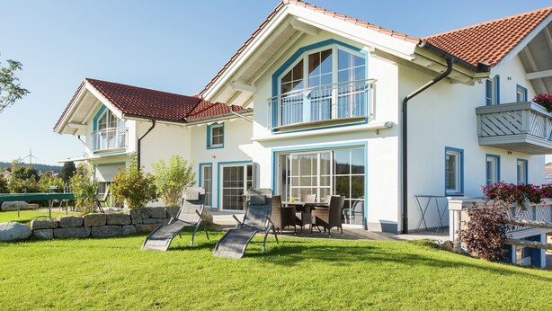 A two-story house with a large balcony, a patio with outdoor furniture, and a well-maintained lawn.