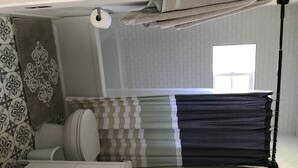 Une salle de bain avec des toilettes, un porte-serviettes avec des serviettes pliées, une serviette à motifs et une fenêtre.