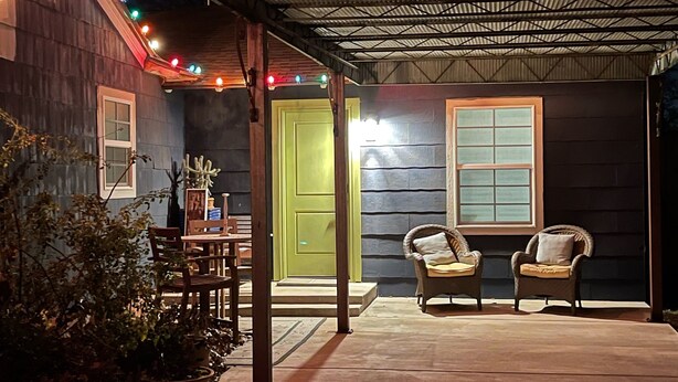Un patio couvert avec une table et des chaises, une porte verte et des guirlandes lumineuses.