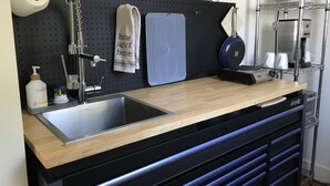Une cuisine avec un panneau perforé noir, un plan de travail en bois, un évier et une machine à café.