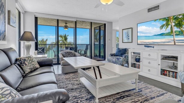 Un salon moderne avec un canapé en cuir, une table basse blanche et un grand téléviseur posé sur un meuble blanc.