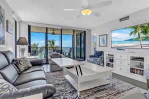 A modern living room with a leather sofa, a white coffee table, and a large TV on a white cabinet. - Beachfront Paradise - Fall Special - Updated Luxury 3rd Floor Condo! (Naples)