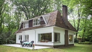 Une maison à deux étages avec une grande véranda à l’avant, une cheminée et un jardin.