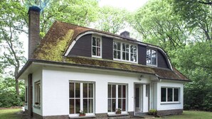 Une maison à deux étages, dotée d’un toit à forte pente, de grandes fenêtres et d’une cheminée en briques.
