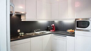 Une cuisine moderne avec des meubles blancs, un plan de travail noir, une machine à café rouge, un four à micro-ondes et un panier de fruits.