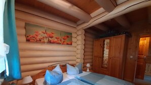 A log cabin bedroom with a bed, pillows, a nightstand, a lamp, a painting, and a wooden wardrobe. - Family Getaway in Dankerode (Harzgerode)