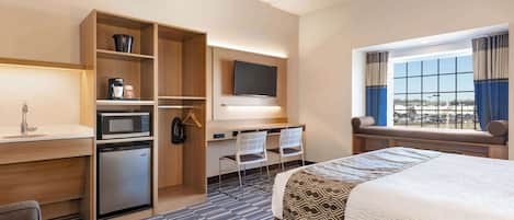 A hotel room with a bed, a desk with a computer, a microwave, a mini-fridge, and a TV.