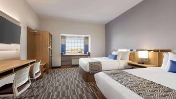 A hotel room with two beds, a desk with chairs, a window with curtains, and a view of the city.