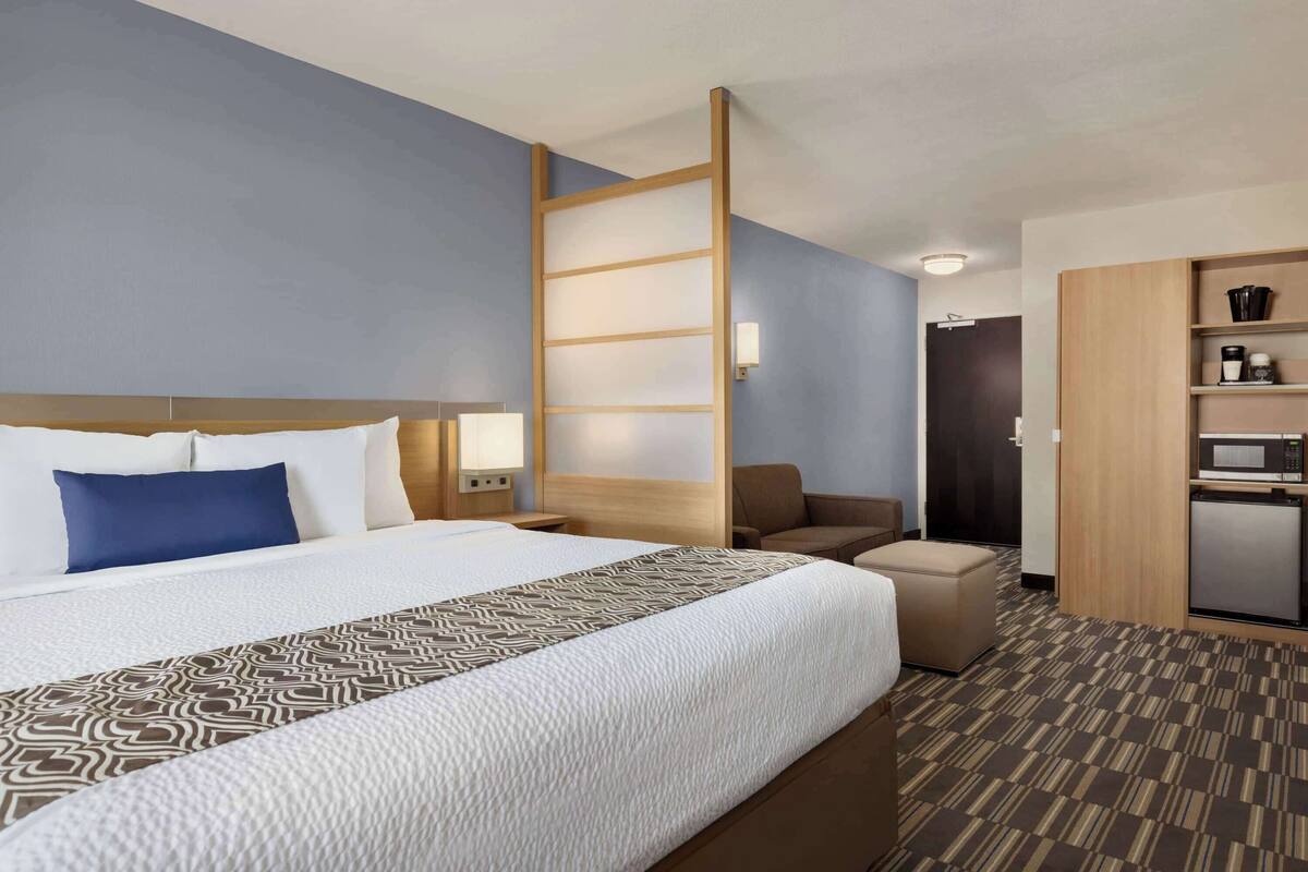 A hotel room with a large bed, a desk, a chair, a microwave, and a small kitchenette.