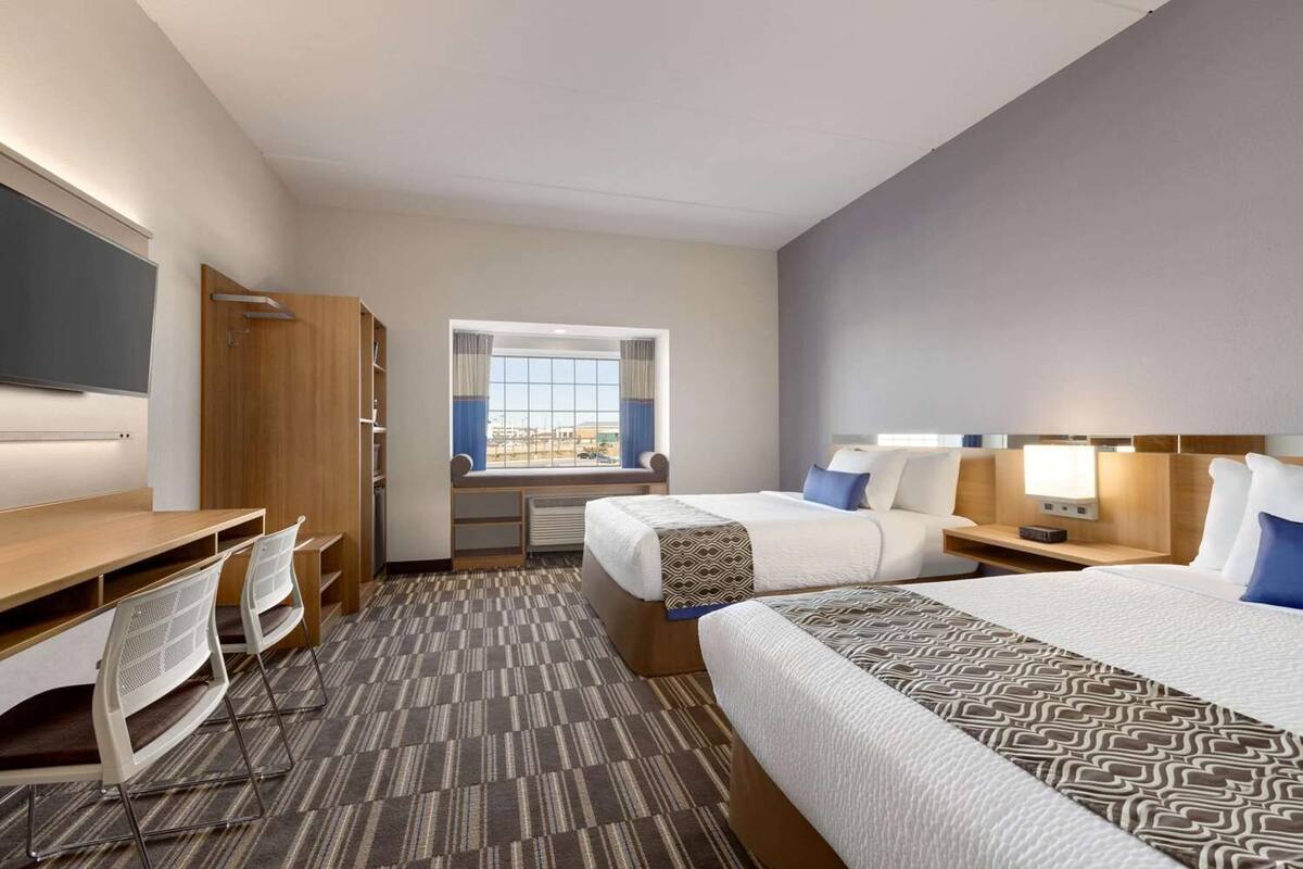 A hotel room with two beds, a desk, a chair, a TV, and a window with curtains.