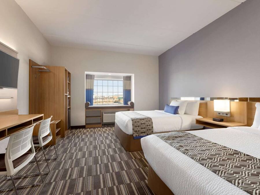 A hotel room with two beds, a desk, a chair, a TV, and a window with curtains.
