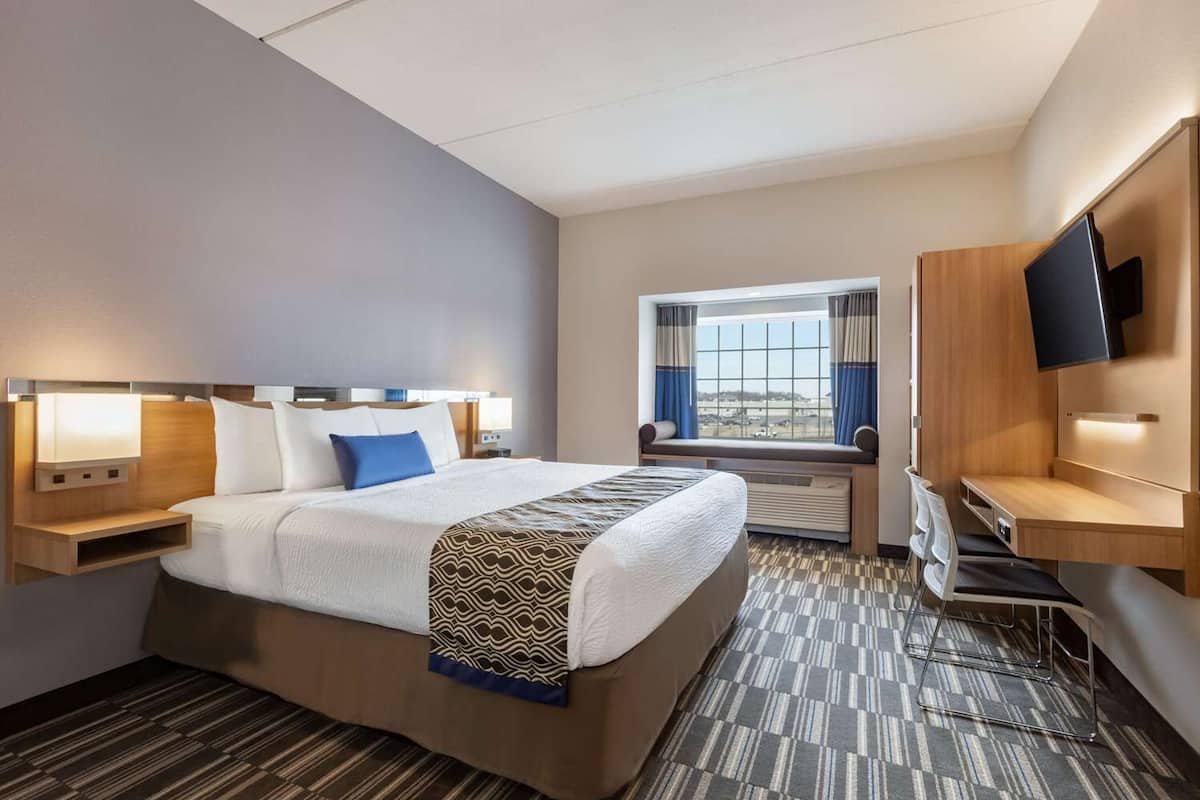 A hotel room with a large bed, a desk, a TV, and a window with a view.