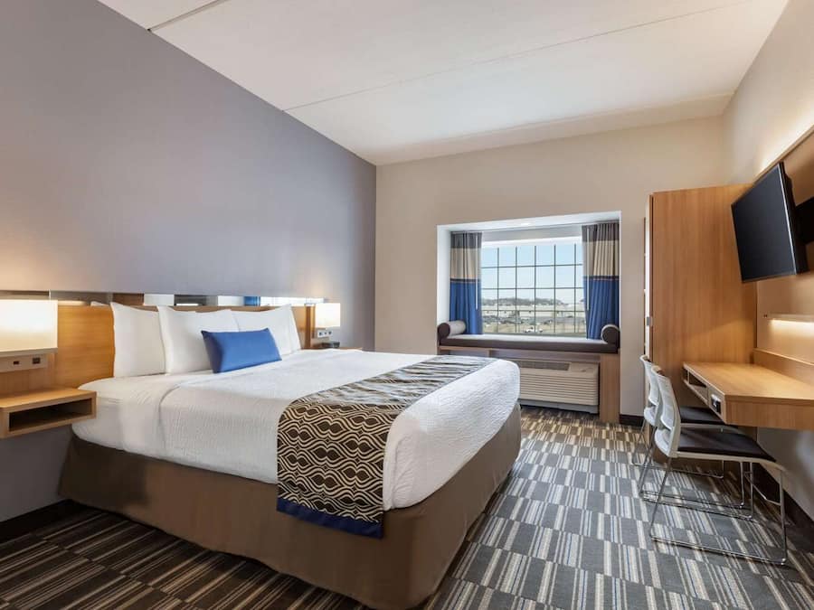 A hotel room with a large bed, a desk, a TV, and a window with a view.