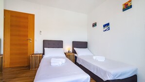 Ein Hotelzimmer mit zwei Einzelbetten, einer Holztür, einem kleinen Nachttisch mit Lampe und zwei Wandbildern.