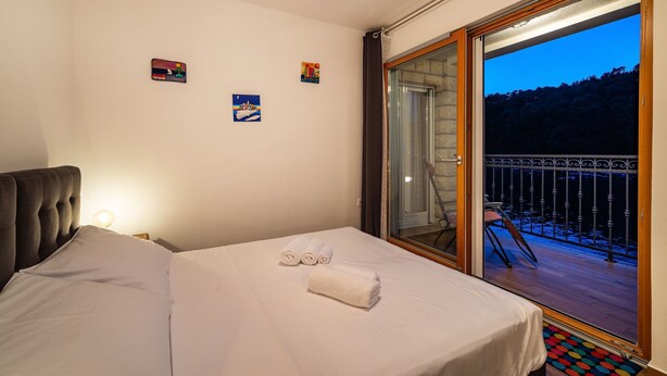 Ein Hotelzimmer mit einem Bett, zwei Bildern an der Wand und einem Balkon mit Blick auf Bäume.