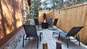 Een houten terras met een vuurkuil, vier stoelen en een tafel.
