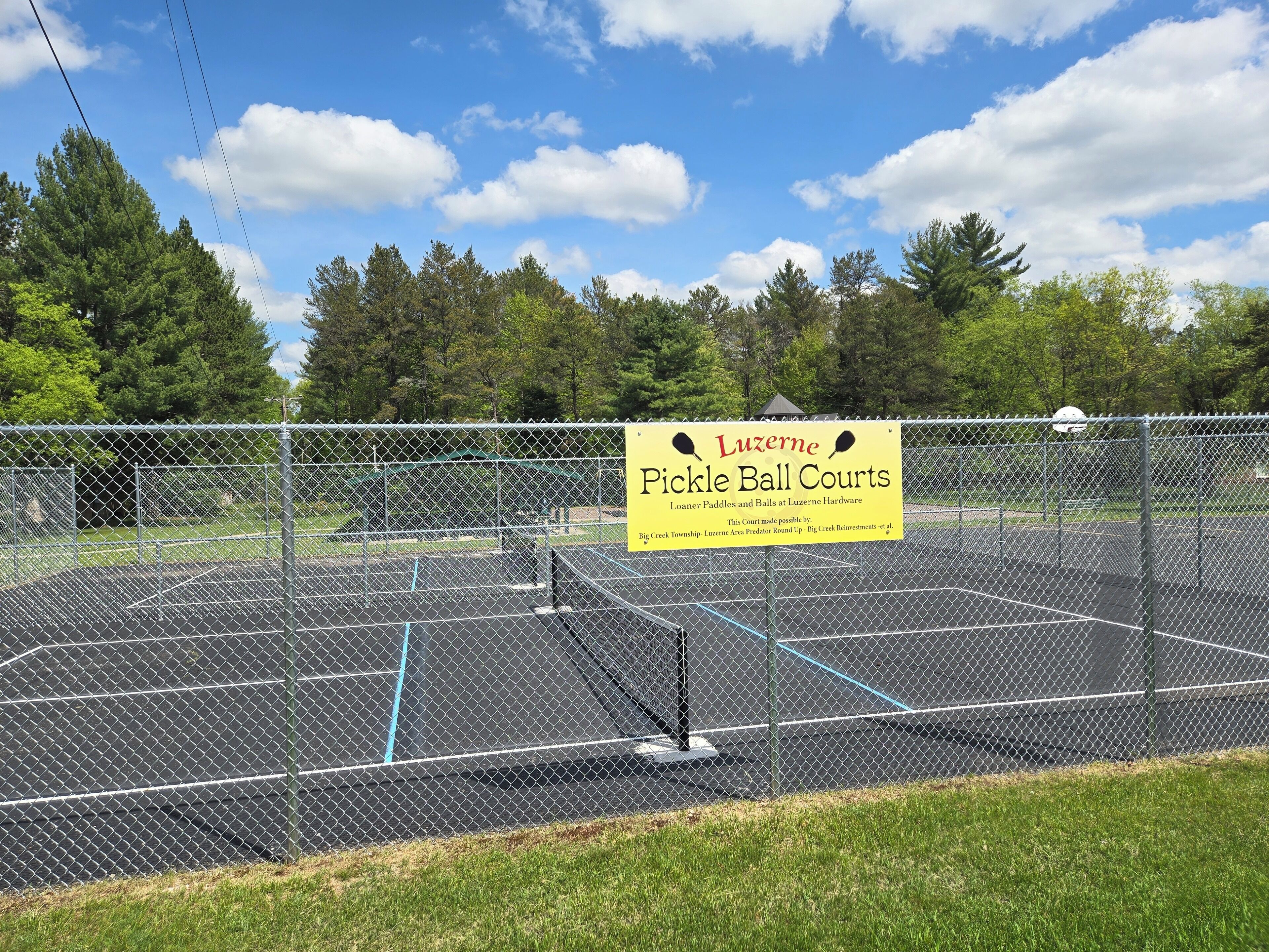 Una cancha de pádel vallada con un letrero que anuncia equipos Luzerne Hardware.