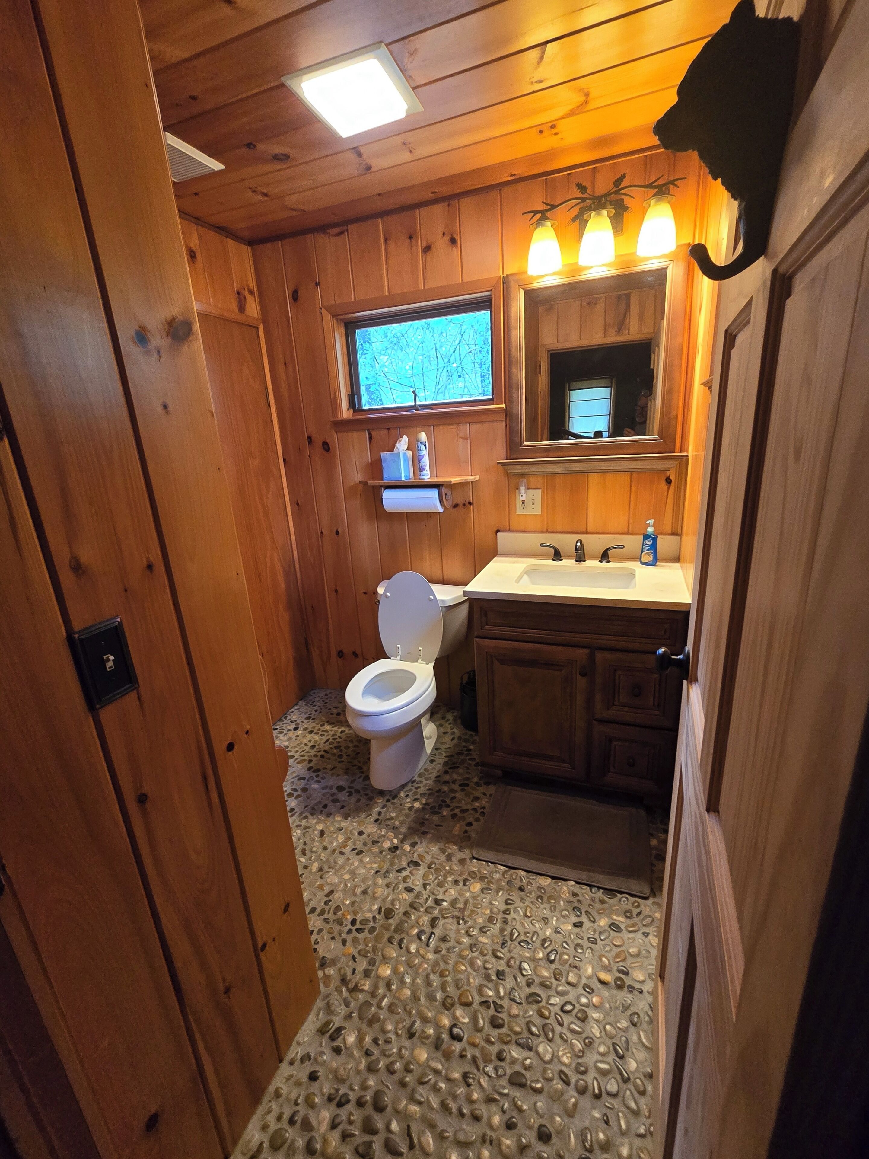 Un baño de cabaña de madera con inodoro, lavabo y espejo.