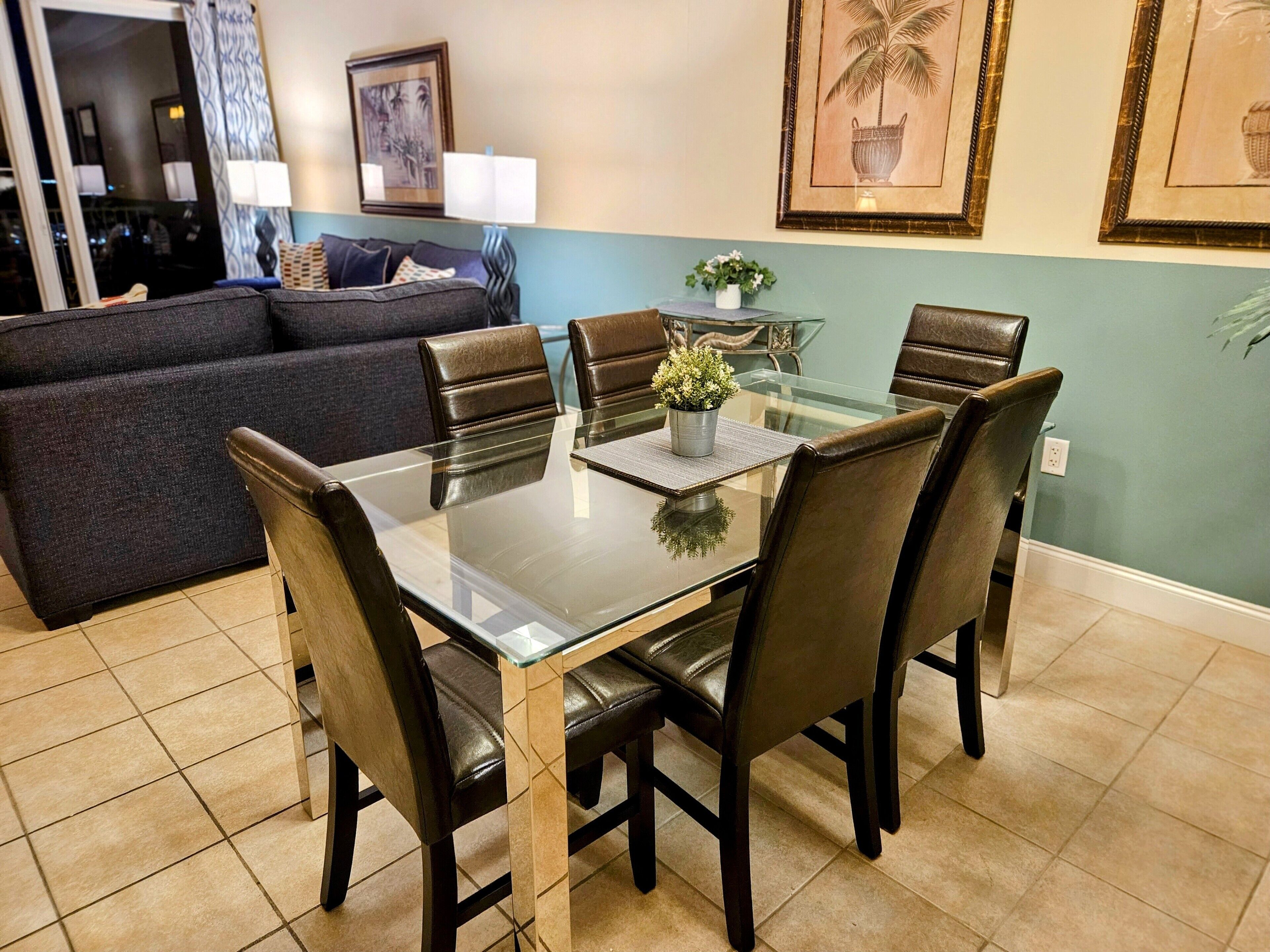 Comedor con mesa de vidrio, seis sillas y una planta en maceta.